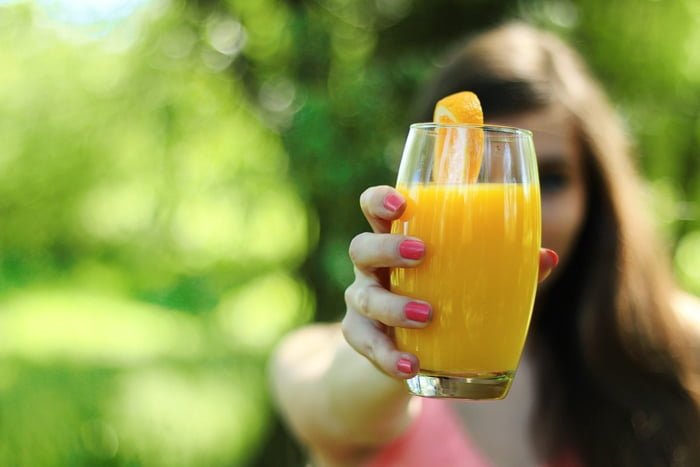 Mulher segura um copo de suco de laranja - Metrópoles