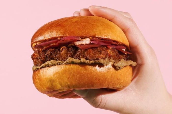 foto de um hamburguer segurado em uma mao com fundo rosa