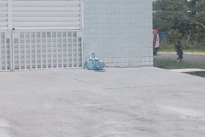 Bolsa azul clara deixada em portão branco. Foto colorida