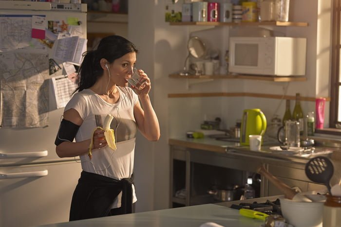 Imagem de mulher comendo na cozinha antes de correr - Metrópoles