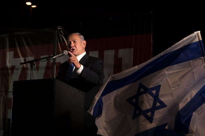 Foto colorida mostra primeiro-ministro Benjamin Netanyahu e uma bandeira de Israel