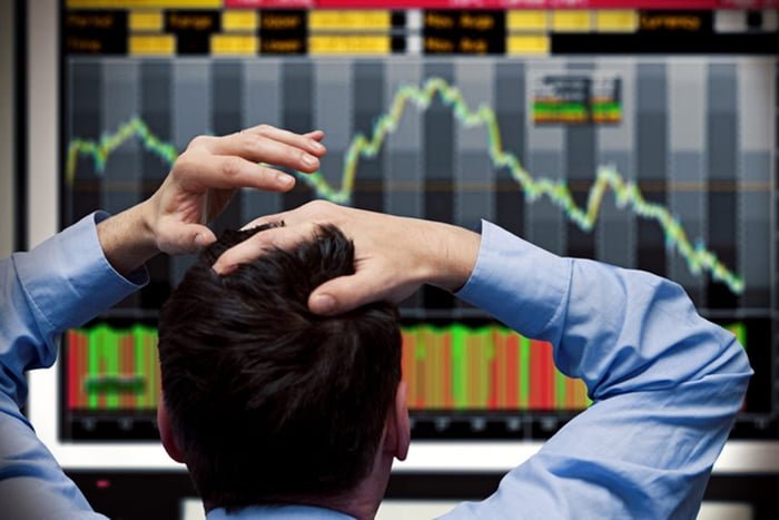 Imagem colorida de homem com mão na cabeça, olhando para um painel com gráficos indicando desempenho de ações da bolsa de valores - Metrópoles