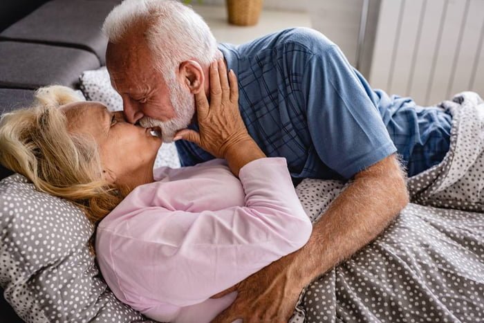 Casal mais velho deitado na cama se beijando - Metrópoles