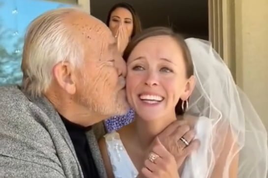 Imagem colorida: pai beija bochecha de filha vestida de noiva - Metrópoles