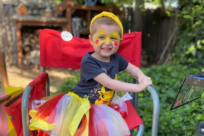 Foto colorida de criança de 4 anos com vestido colorido, faixa no cabelo e rosto pintado - Metrópoles