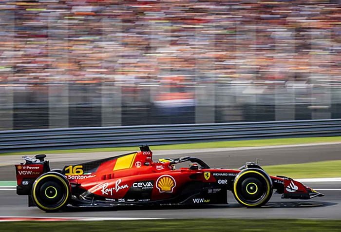 Imagem colorida de Ferrari vermelha em alta velocidade enquanto torcida embaçada torce no fundo da foto - Metrópoles