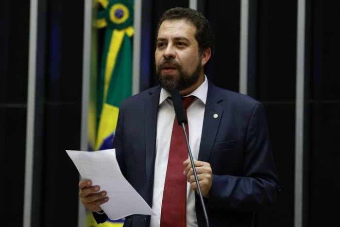 Imagem colorida mostra Guilherme Boulos, homem branco, de cabelo e barba castanhos, de terno azul, camisa branca e gravata vermelha, falando ao microfone no plenário da Câmara dos Deputados - Metrópoles