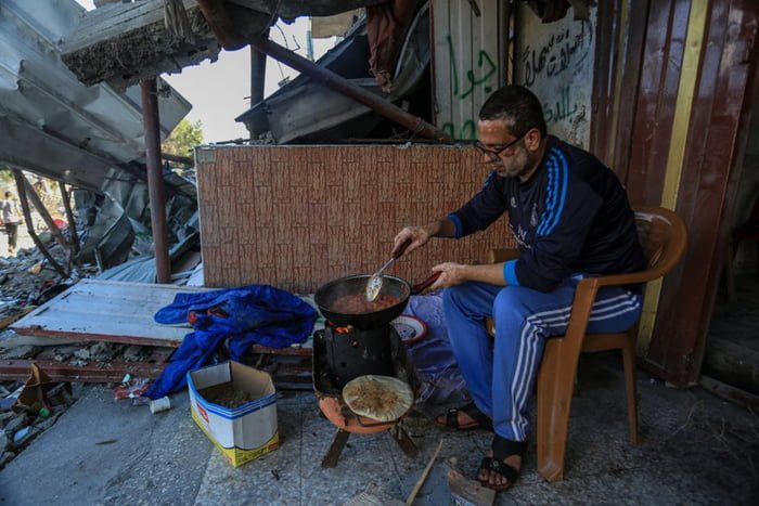 Imagem colorida mostra Homem cozinha em fogueira improvisada em meio a destroços em Gaza - Metrópoles