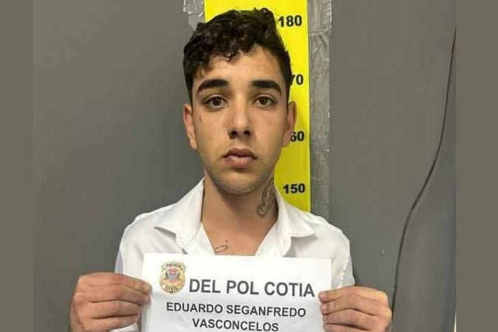 Imagem colorida mostra Eduardo Seganfredo preso. Ele é um jovem branco, com tatuagem no pescoço, e segura a placa com sua identificação - Metrópoles