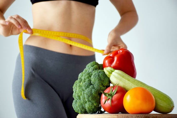 mulher medindo gordura abdominal e alimentos no primeiro plano