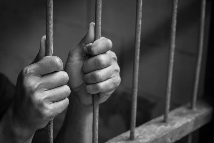 Imagem em preto e branco mostra mãos de segurando grades na cadeia condenado / saidinha - Metrópoles