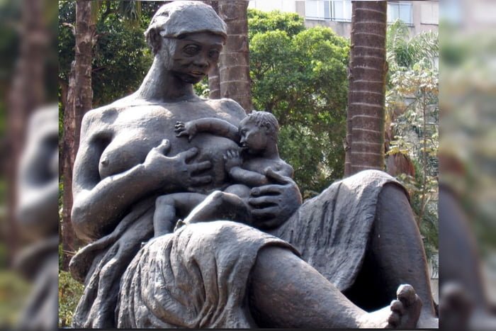 Foto colorida da escultura Mãe Preta, que mostra uma figura feminina amamentando um bebê