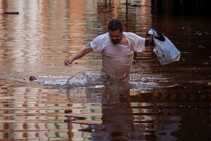 Imagem colorida de homem atravessando enchente em Porto Alegre - Metrópoles