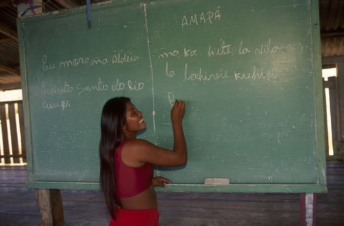 Imagem colorida de mulher indígena sendo alfabetizada - Metrópoles