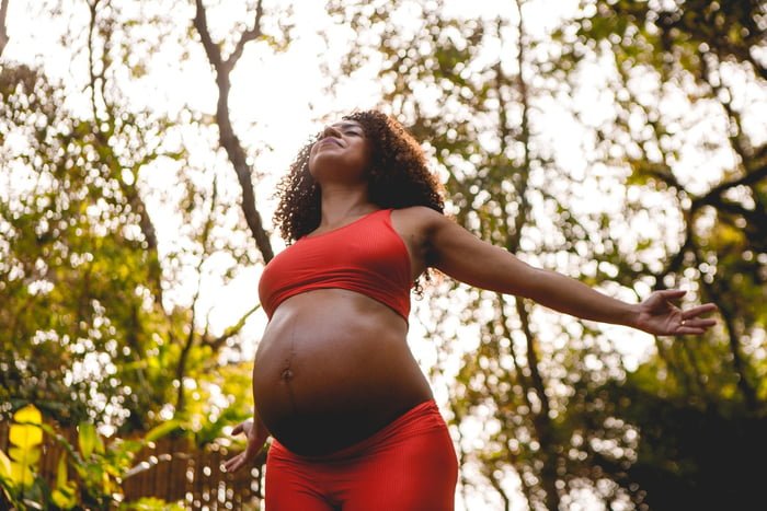 Foto de mulher negra grávida fazendo atividade fisica - yoga ao ar livre - Metrópoles