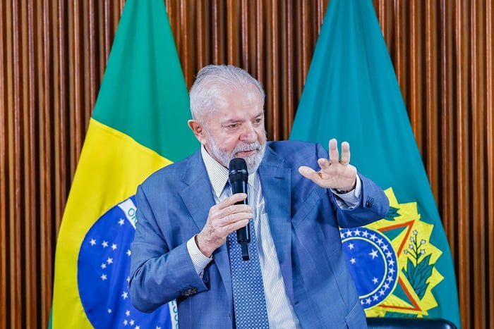 Presidente Lula no Palácio do Planalto, em frente à bandeira do Brasil, com microfone e mão estendida - Metrópoles