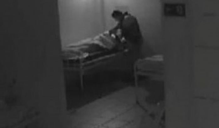 Foto em preto e branco de vigilante colocando a mão em baixo da coberta em que a paciente estava - Metrópoles
