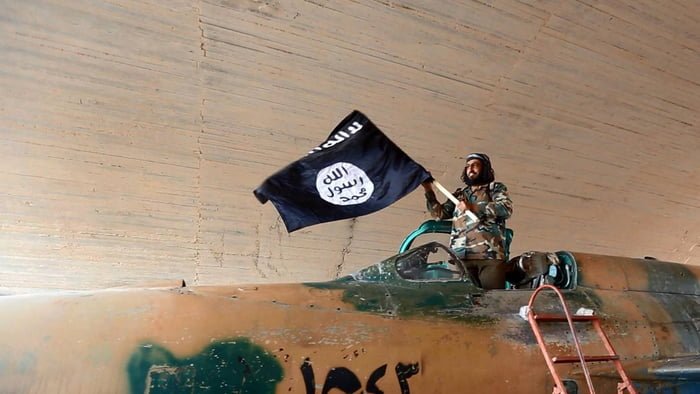 Imagem colorida mostra membro do Estado Islâmico em cima de um tanque segurando uma bandeira do grupo - Metrópoles