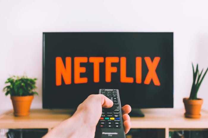 Homem apontando controle remoto para a TV com uma logo da Netflix