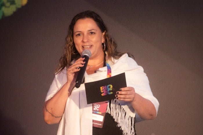 Foto colorida - Irina Neves, mulher branca com microfone na mão
