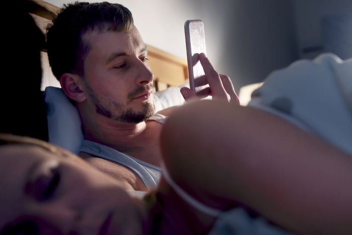 casaç heterossexual na cama com o homem mexendo no telefone